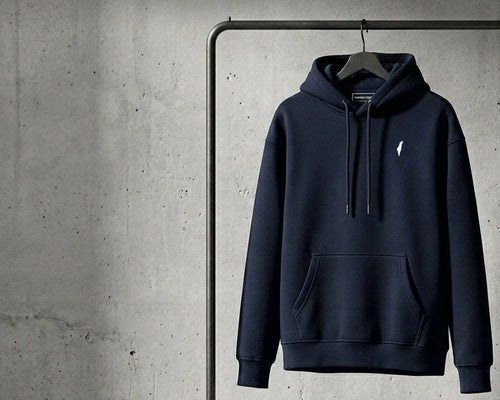 A dark navy blue pullover hoodie with a small white embroidered Polo Ralph Lauren logo on the left chest, hanging on a black clothing rack against a textured gray concrete wall.