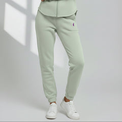 Model wearing sage green Cali Sweatpants with a purple thigh logo and cuffed ankles, styled with white sneakers.