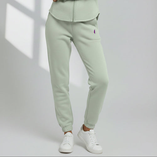 Model wearing sage green Cali Sweatpants with a purple thigh logo and cuffed ankles, styled with white sneakers.
