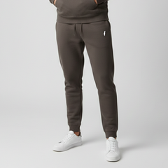 Model wearing dark charcoal Premium Sweatpants with a drawstring waist, white thigh logo and cuffed ankles, styled with white sneakers.